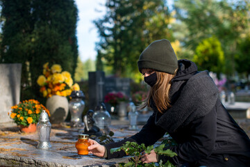 A woman wearing a protective mask against the coronavirus in the cemetery, holding a candle snitch...