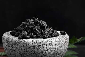 Close up of black raisins in a stone bowl, close up, dark background