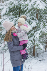 Little girl with mother walking in snowy forest in winter.