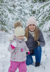 Fototapeta premium Young woman and little girl walking in the snowy forest and playing snowballs.