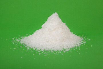 Coarse granules of natural rock or sea salt on green background.