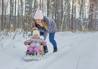 Fototapeta na wymiar Little girl and young mother enjoy sleigh ride in snowy forest.