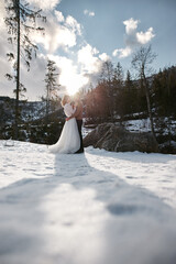 newlyweds bride and groom kissing in snow park during winter. woman wears minimalist white wedding dress. man wears casual clothing