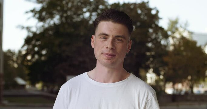 Young guy teen talking looking at camera while standing outdoors on street in city. Portrait of male student wears white stylish t-shirt clothes speaks smiling, web cam view, communication concept