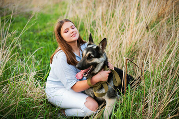 Cute teenage girl hugging Eastern European Shepherd in the field. Smiling young woman enjoying good day and posing with pet
