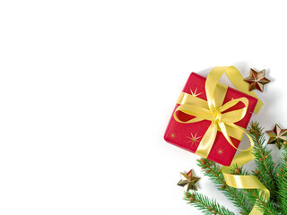 The gift wrapped in red wrapping paper is tied with a yellow ribbon with a bow. A natural spruce branch and golden stars are nearby. Christmas composition. Flat lay. Top view. Copy space.