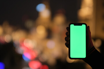 close up one hand holding green screen smart phone with colorful city bokeh at night