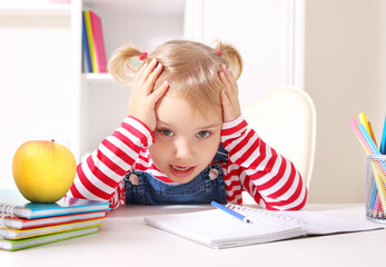 Child tired of school learning.Little girl unhappy face sitting at table.Preschooler...