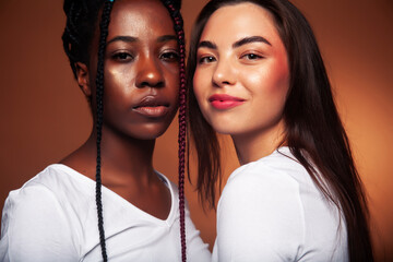 young pretty caucasian, afro woman posing cheerful together on brown background, lifestyle diverse...