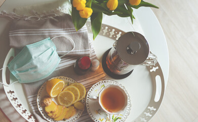 Plate of tea, lemon and ginger on bed table with yellow tulips
