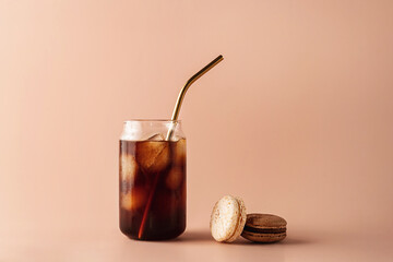 Glass of iced coffee in tall glass with golden straw with cream and macaroons chocolate, vanilla on...