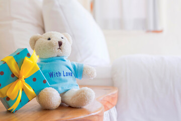 Cute toy bear with gift box on background blur white bed sheets and pillows and leave space for adding your content.