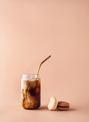 Glass of iced coffee in tall glass with golden straw with cream and macaroons chocolate, vanilla on...