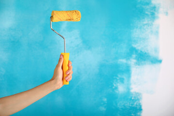 close up of female hand holding paint yellow roller over blue background-repair, construction and building tools concept. Convenient and versatile tool for painting walls.