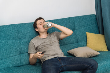 a young man with a beer in front of the TV. unemployed man with alcohol alone watching TV