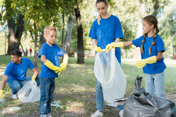 Family collecting rubbish into recycled bags in forest, ecology concept