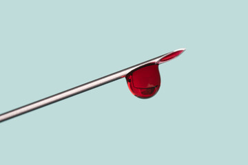 drop of blood on the tip of a syringe needle over light blue background