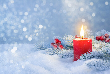 Burning candle in snow with festive decoration over frosty background