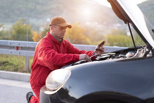 Handsome auto mechanic or road assistance worker in uniform repairing engine of the broken car on the road