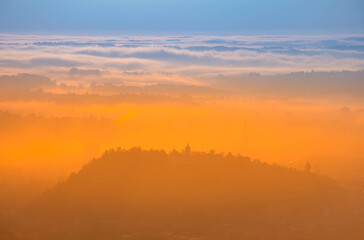 Amazing foggy sunrise over the city of Graz with Schlossberg hill and Church of the Sacred Heart of Jesus tower, in Styria region, Austria. Panoramic view from Plabutsch mountain on autumn morning.