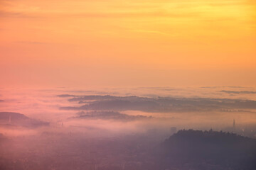 Amazing foggy sunrise over the city of Graz with Schlossberg hill and Church of the Sacred Heart of Jesus tower, in Styria region, Austria. Panoramic view from Plabutsch mountain on autumn morning.