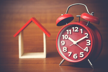 red clock and miniature house on wooden background, copy spaсe.