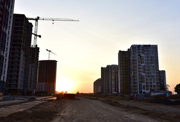 Fototapeta premium View on the large construction site with tower cranes and buildings on sunset background. Road work and Dig pit foundation. Out of focus, possible granularity, motion blur