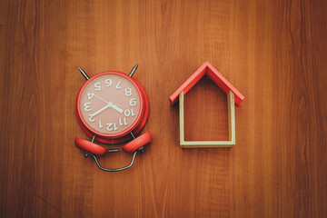 red clock and miniature house on wooden background, copy spaсe.