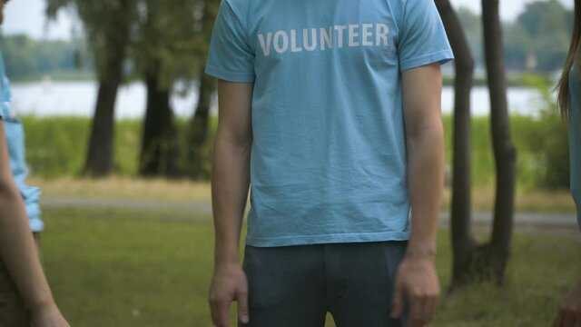 Handstack of unrecognizable young volunteers outdoors. Confident satisfied Caucasian people stacking hands on clear summer meadow in park. Environmental cleanup.