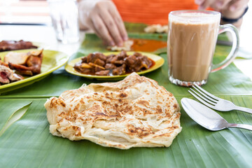 Roti canai or paratha served on banana leaf, with mutton curry and fried chicken, and popular teh...