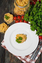 table setting with white plate, pasta and vegetables on a wooden table, vertical