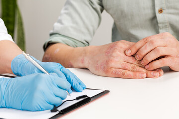 A gloved dermatologist examines the skin of a sick patient and records observations. Examination...