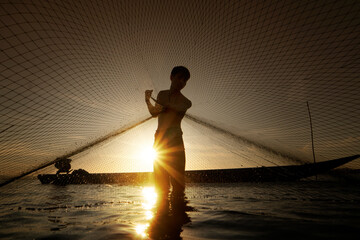 Fisherman throwing out fishing net on the lake with sun background