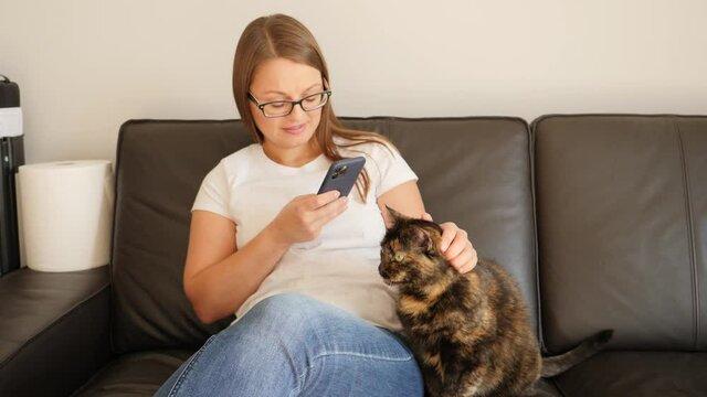 Woman takes pictures via smartphone of her pet animal strokes a cat sitting on a couch at home