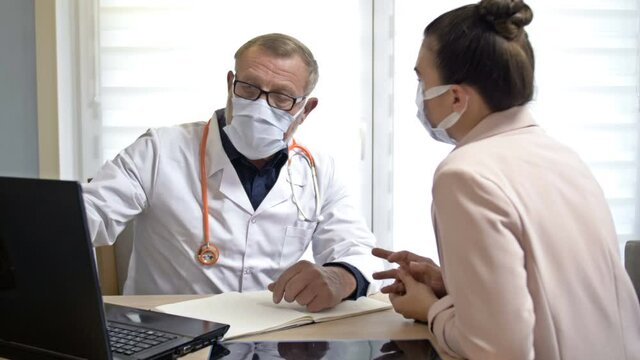 An experienced male doctor consults a female patient. Doctor and patient wearing medical masks. Action to be taken during the COVID-19 pandemic.