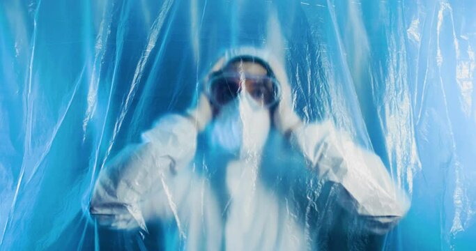 Medico o infermiere con tuta bianco covid si mette le mani in testa dalla disperazione dietro a un telo di plastica trasparente in ospedale.