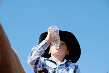 Young cowboy drinking water close up while riding horse, western lifestyle hydration concept.