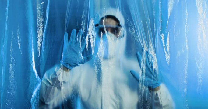 Medico o infermiere con tuta bianco covid si mette le mani in testa dalla disperazione dietro a un telo di plastica trasparente in ospedale.