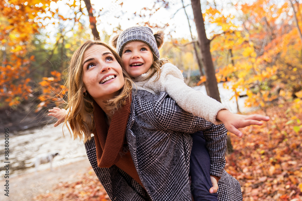 Wall mural little girl and her mother playing in the autumn park with child on back