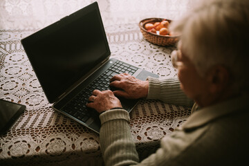 Fototapeta na wymiar Close-up of senior grandmother's hand typing messages on laptop keyboard to her family during quarantine COVID - 19 coronavirus