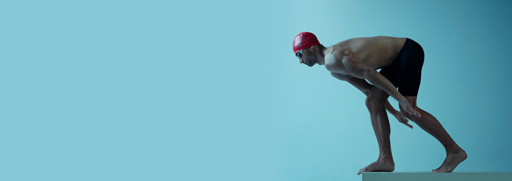 Professional caucasian male swimmer practicing and training isolated on blue neoned studio background. Grace of motion and action. Healthy lifestyle, sport and movement concept. Flyer with copyspace.