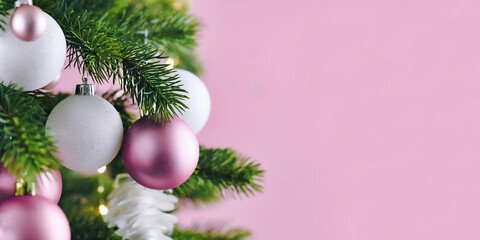 Fototapeta na wymiar Banner with Christmas tree decorated with white and pink seasonal tree ornament baubles on pink background with empty copy space