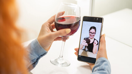The women talk over video communication on the phone and drink red wine. The quarantined girl is not making a video call