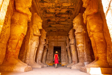 A young woman in red dress looking at the pharaohs at the Abu Simbel Temple in southern Egypt in...