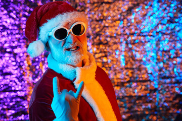 Portrait of Santa Claus in red costume and sunglasses posing at camera against the shiny background