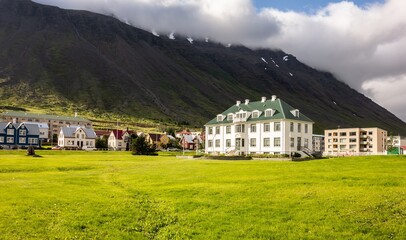 White Isafjordur Culture House on a green meadow at sunny day with storm coming