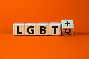 Dice form the acronyms 'LGBTQ' and 'LGBT+'. Male hand. Beautiful orange background. Concept, copy space.