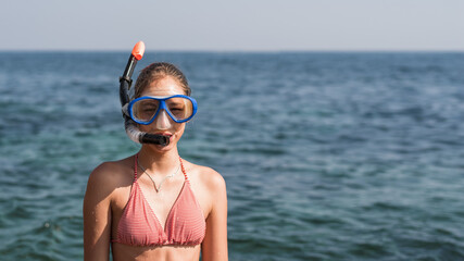 Happy baby girl in mask and snorkel on the beach in summer with sea background