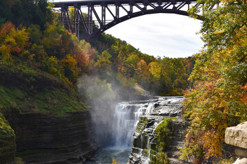 A waterfall with fall foliage and a bridge overhead