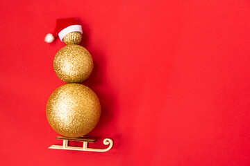 Christmas snowman made of golden Christmas balls of different sizes on a red background. Santa's red hat on a snowman, and rides on a sled. Christmas creative. Copy space